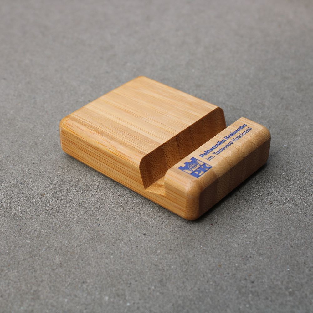 bambusowa podstawka pod telefon z jasnego drewna z granatowym logo Politechniki Krakowskiej