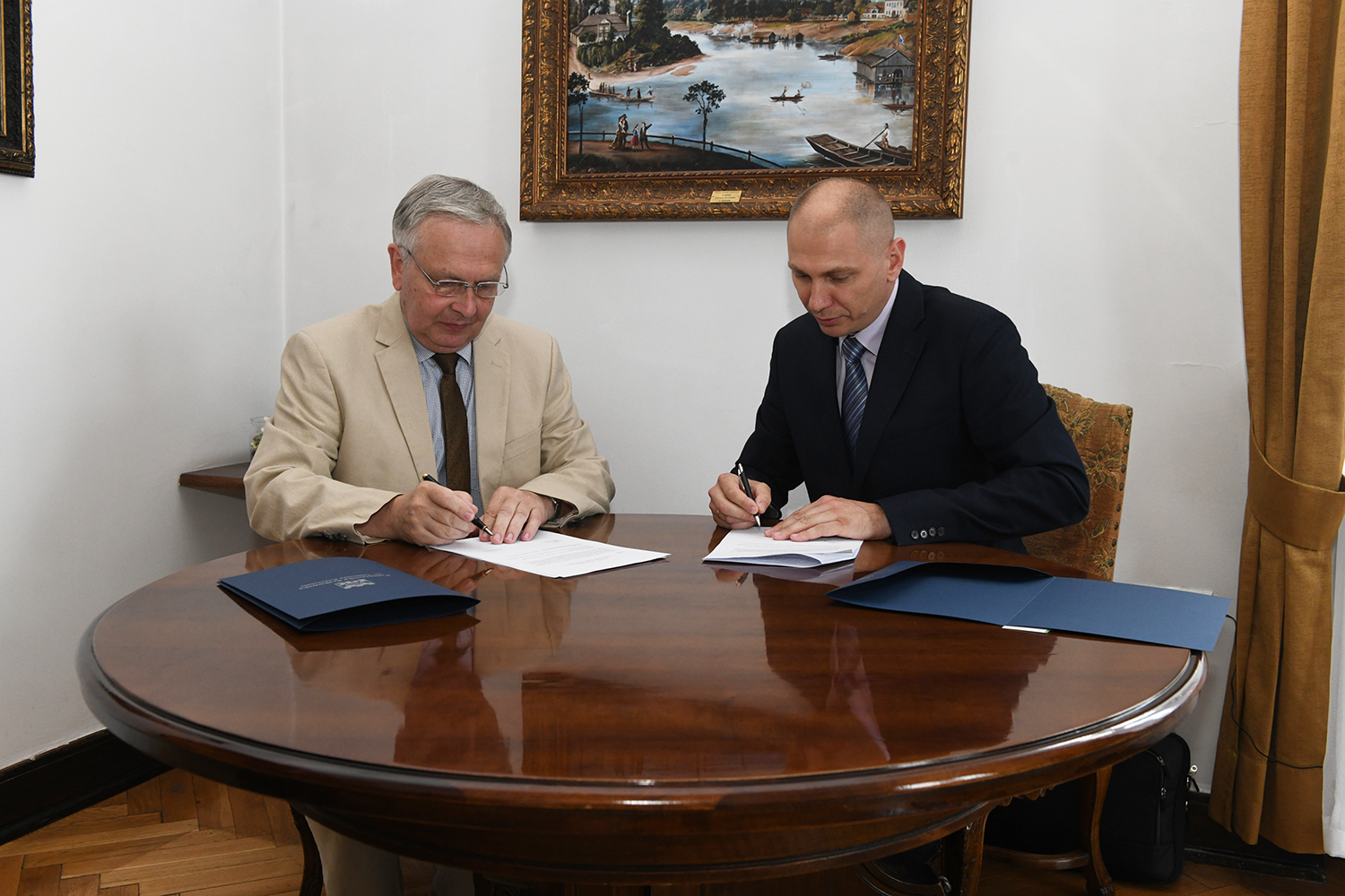 Przy stole siedzą dwaj mężczyźni. Jednym z nich jest rektor Politechniki Krakowskiej, a drugim Sebastian Talarczyk, członek Zarządu FAKRO. Panowie podpisują dokumenty.