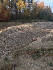 Na zdjęciu teren kopalni diatomitu na Podkarpaciu: wyrobisko w postaci dziury w ziemi. W tle drzewa z jesiennymi liśćmi w różnych kolorach i fragment nieba