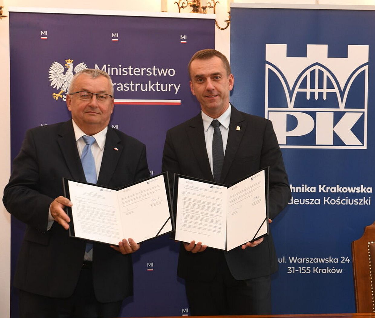 Minister Adamczyk i rektor Szarata pozują do zdjęcia trzymając otwarte teczki z umową