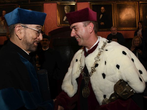 Rektor Andrzej Szarata w czerwonej todze z gronostajowym kołnierzem ściska dłoń mężczyźnie w czarno-niebieskiej torze i z brodą w okularach. Ten mężczyzna to profesor Bonenberg.
