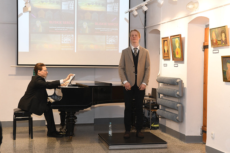 Mężczyzna siedzi przy fortepianie, a młody chłopak stoi przed instrumentem