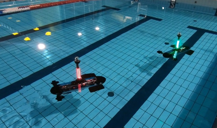 Pojazdy biomimetyczne pływają w basenie. Jeden daje zielone, a drugi czerwone sygnały świetlne