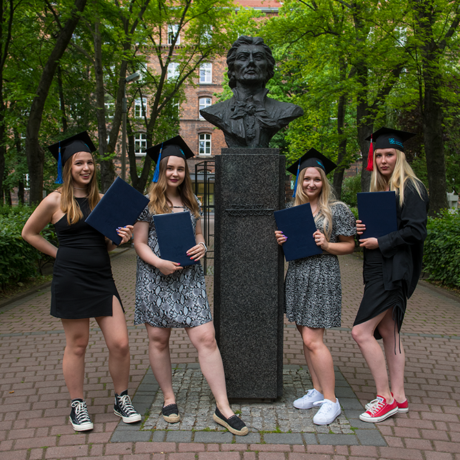 cztery młode dziewczyny w biretach i z dyplomami w dłoniach pozują do zdjęcia pod popiersiem Tadeusza Kościuszki na dziedzińcu Politechniki Krakowskiej.