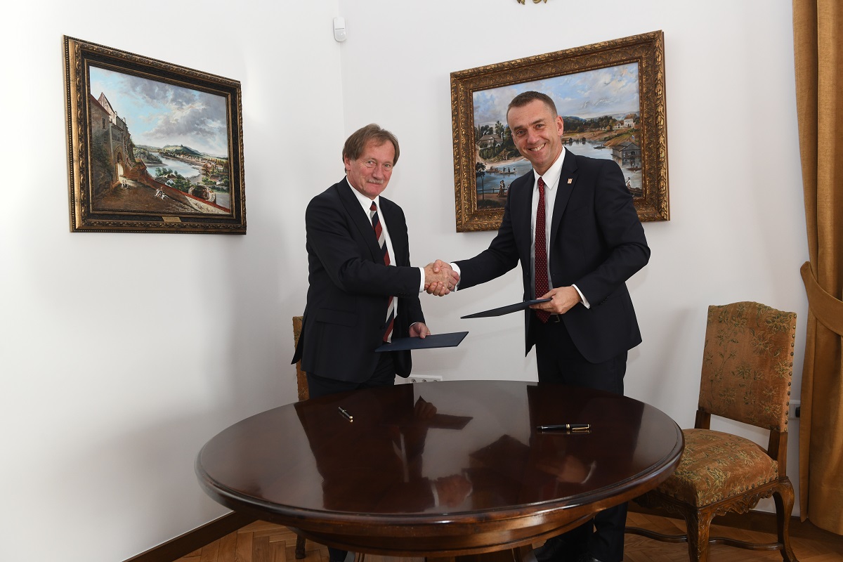 Mirosław Boryczko i prof. Andrzej Szarata podają sobie dłonie, a w drugiej ręce trzymają podpisane umowy. Na twarzach uśmiechy