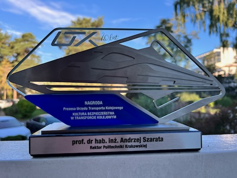 Szklana statuetka o nieokreślonym kształcie na postumenciku z napisem wskazującym na kategorię nagrody oraz nazwiskiem laureata