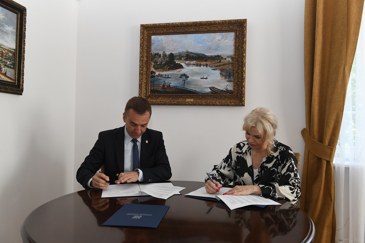Rektor PK prof. Andrzej Szarata i dyrektor ZDMK Magdalena Nowak-Obrzut siedzą przy stole i podpisują porozumienie