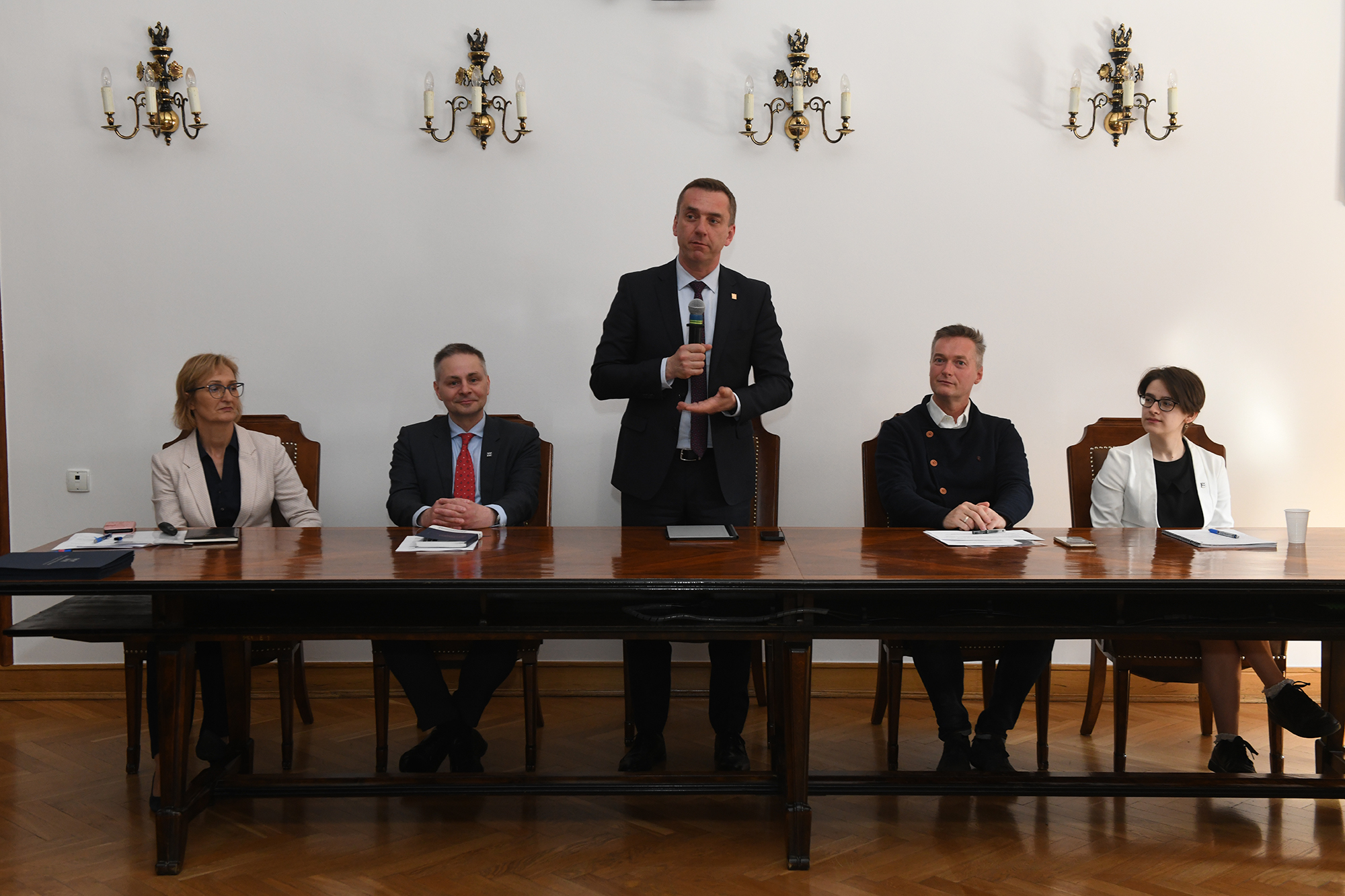 Stół prezydialny, w środku stoi i przemawia rektor PK prof. Andrzej Szarata, dwie osoby siedzą po jego lewej i po prawej stronie