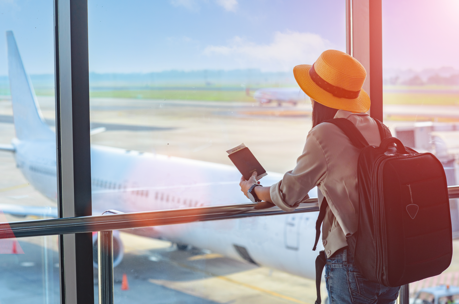 Dziewczyna z paszportem w ręku i dużym plecakiem patrzy na znajdujący się na płycie lotniska samolot
