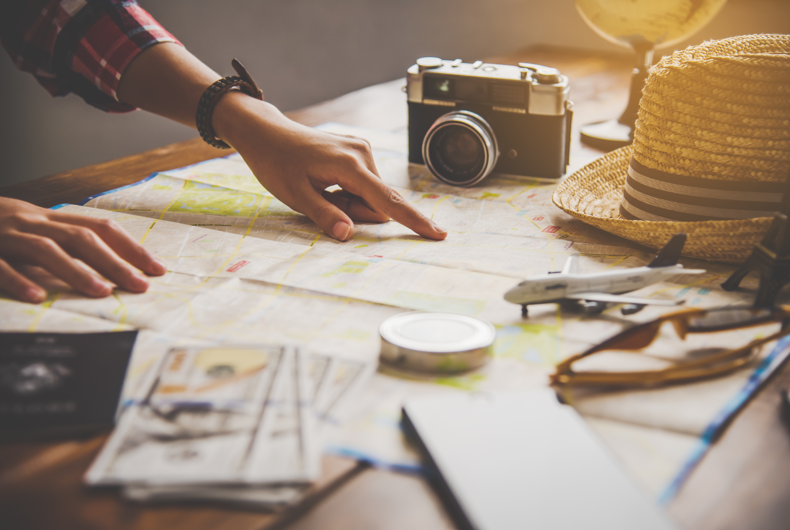 Na sole leży mapa, apart fotograficzny, kapelusz i rózne drobiazgi kojarzace się z podróżą. Ktoś palcem wskazuje wybrane miejsce na mapie.